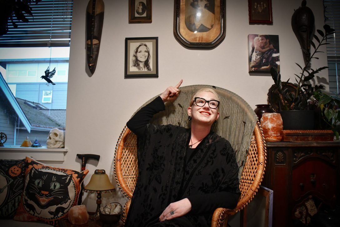 Olexia sitting in her Capitol Hill home, pointing upwards at her framed photo collection.